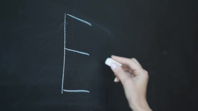 Teacher is writing letter of alphabet on blackboard with chalk. Education in elementary school concept.