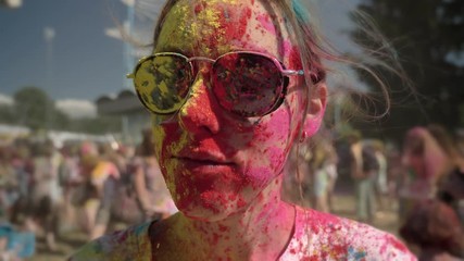 Young happy girl in colourful powder is wearing sunglasses on holi festival in daytime in summer, color concept