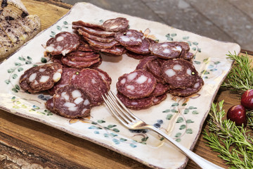 Italian flavors: sliced salami in a plate placed on a wooden table decorated with oregano and cherries - selective focus