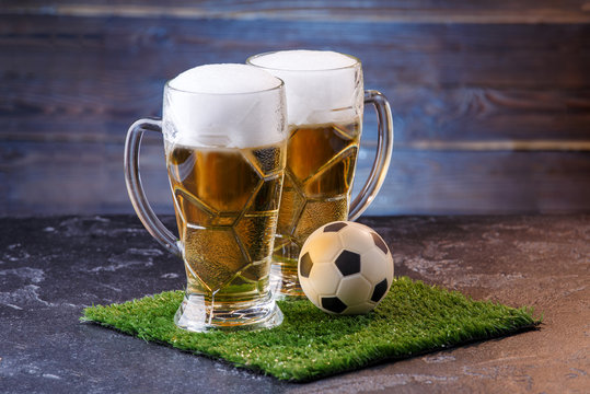 Photo of two glasses of beer, soccer ball on green grass
