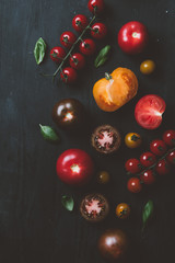 top view of black prince tomatoes and cherry tomatoes with basil leaves on black wooden background