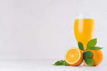Fresh vitamin yellow summer beverage of ripe oranges with green leaves on light white wood background.