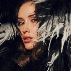 Portrait of young beautiful brunette woman wearing elegant faux fur coat with long black and white hair. Gorgeous sexy caucasian female model with evening makeup posing with raised crossed arms.