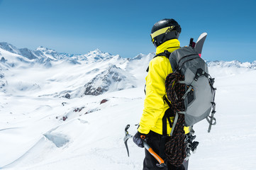 A mountaineer man holds an ice ax high in the mountains covered with snow. View from the back. outdoor extreme outdoor climbing sports using mountaineering equipment
