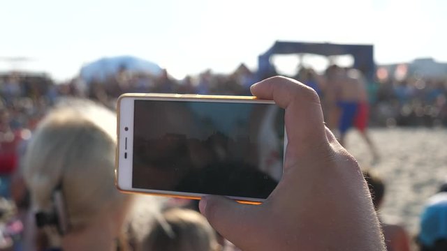 Closeup man hand holds a mobile shoot with phone camera an event in public place