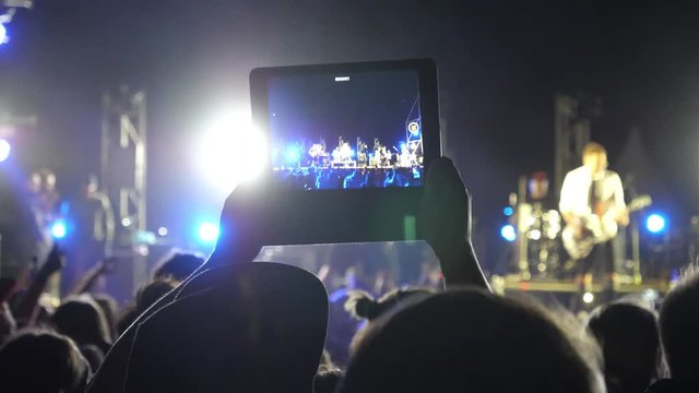 Hold tablet fan in concert people crowd shoot video streaming at night open air