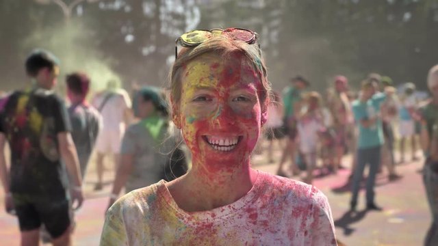 Young happy girl in colourful powder is smiling on holi festival in daytime in summer, watching at camera, color concept, emotional concept