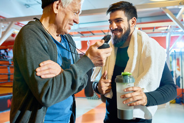 Cheerful elderly coach and bearded man taking rest after workout and chatting happily. 