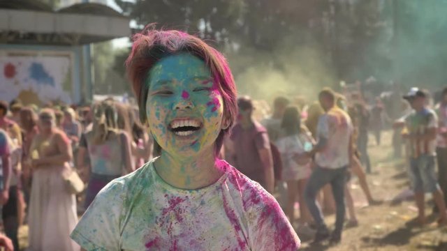 Young happy asian girl is raising hands on holi festival in daytime in summer, watching at camera, color concept, emotional concept