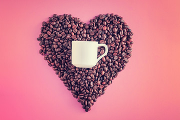 coffee beans in shape of heart and white cup on pink background