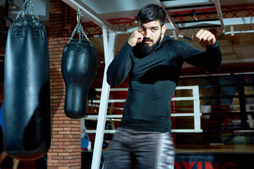 Bearded brutal man in gym practicing boxing attack and punch looking confidently. 