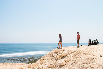 couple on vacation walking on cliff with ocean view, motorbike