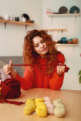 Crochet thread. Appealing ginger-haired girl wearing bright red sweater holding thick maroon crochet thread