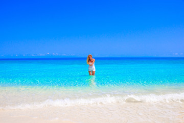 Fototapeta na wymiar Gorgeous blond woman with white clothes is standing in the water at the sandy beach