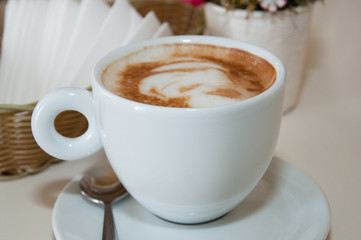 Appetizing coffee cappuccino in a white cup on the table in a cafe