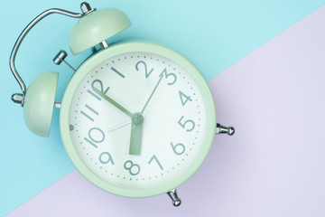 Vintage alarm clock on sweet pastel colored paper top view, background texture, pink, purple, yellow, beige, green and blue colour.