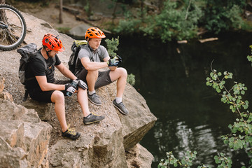 high angle view of friends cyclists with backpacks resting with sport bottle of water on rocky...