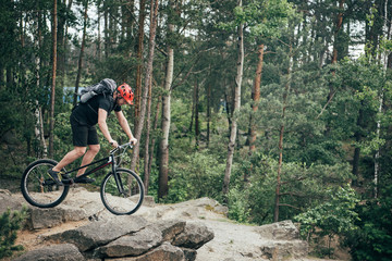 side view of male extreme cyclist in protective helmet doing stunt on mountain bicycle in forest