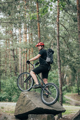 Fototapeta na wymiar male extreme cyclist in protective helmet standing on mountain bicycle on stone in forest