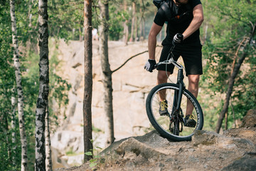 cropped image of male extreme cyclist with backpack doing stunt on bmx in forest