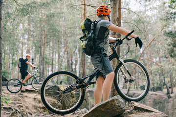 Naklejka premium selective focus of male extreme cyclist on mountain bike talking to friend with bmx in forest