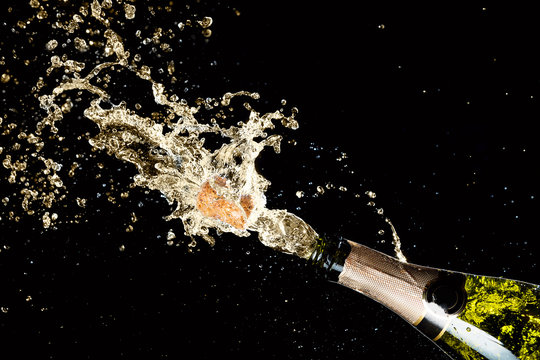 Celebration of birthday, anniversary or Christmas theme. Explosion of splashing champagne sparkling wine with flying cork out of the bottle on black background.