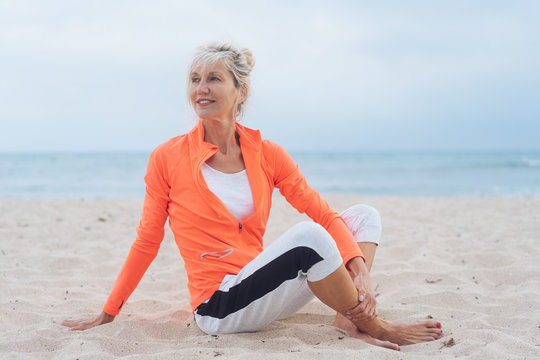 &auml;ltere frau sitz am strand und dehnt sich nach dem sport