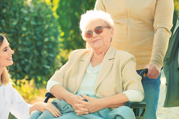 Senior woman in wheelchair with nurse from care home and her friends outdoors