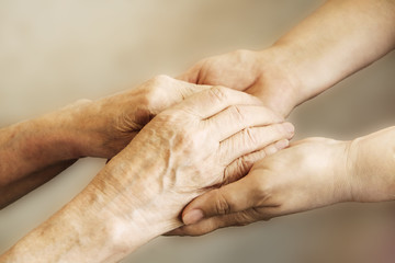 Mature female in elderly care facility gets help from hospital personnel nurse. Senior woman w/ aged wrinkled skin & care giver, hands close up. Grand mother everyday life. Background, copy space.