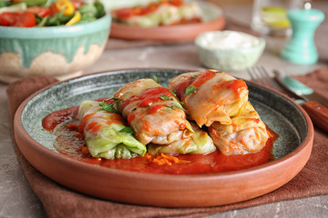Plate with stuffed cabbage leaves in tomato sauce on table