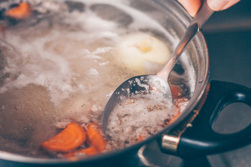 Cook with a spoon removes the foam from the boiling soup in a saucepan
