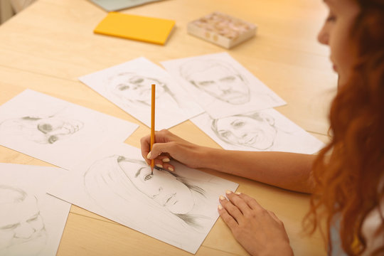 Drawing caricatures. Red-haired appealing creative person feeling extremely cheerful while drawing caricatures