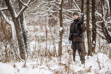 Fototapeta na wymiar Male hunter in camouflage, armed with a rifle, standing in a snowy winter forest with duck prey