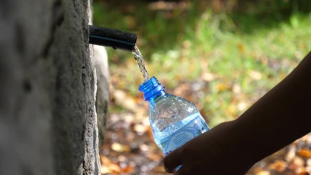 Draw drinking clear pure mountain sourse water in a plastic bottle during walking in nature park in Bulgaria