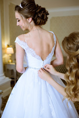 Bridesmaid is lacing white wedding dress for beautiful bride