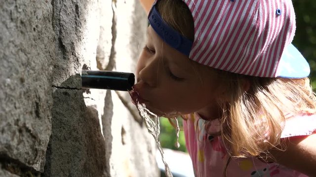 Kid girl bend to quench thirst drink water from mountain clean pure sourse and spit it out