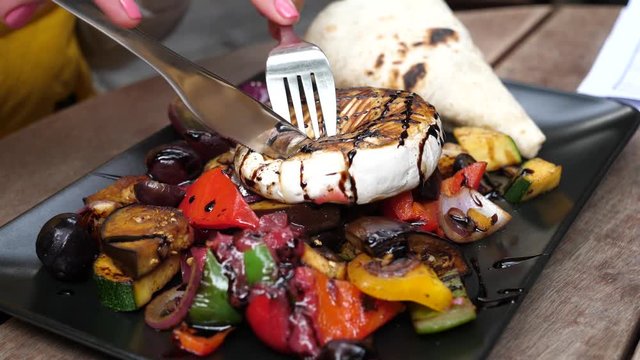 Slicing eating a tasty healthy salad with camembert cheese and grilled vegetables