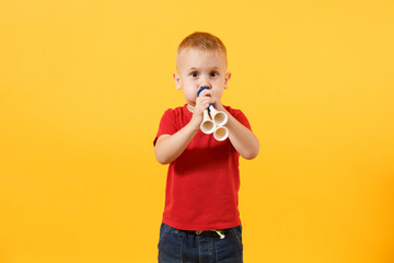 Little cute kid baby boy 3-4 years old, football fan in red t-shirt holding in hand pipe, blowing isolated on yellow background. Kids sport family leisure lifestyle concept. Copy space advertisement.