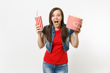 Portrait of young amazed beautiful woman in casual clothes watching movie film, holding bucket of popcorn and plastic cup of soda or cola isolated on white background. Emotions in cinema concept.