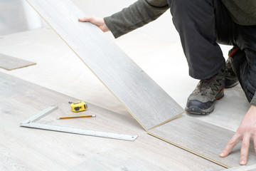DIY, repair, building and home concept - close up of male hands lying parquet floor board/laminate flooring