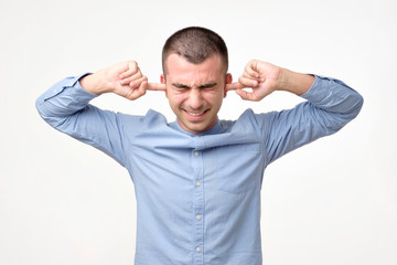 Stressed frustrated young man plugging his ears and keeping eyes closed.