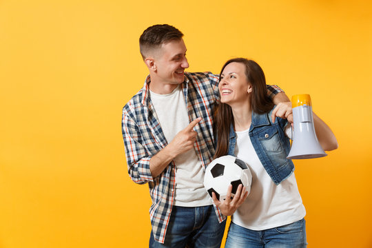 Young happy cheerful couple supporter, woman man, football fans cheer up support team, holding megaphone, soccer ball isolated on yellow background. Sport, family leisure, people lifestyle concept.