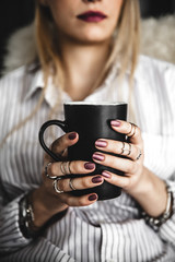 Fototapeta premium Female hands holding a white cup of tea, burgundy manicure, the girl is dressed in a shirt