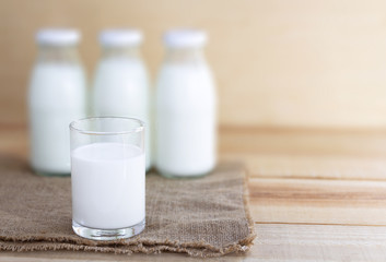 A glass of milk and three bottles of milk placed on sackcloth on a wood table.