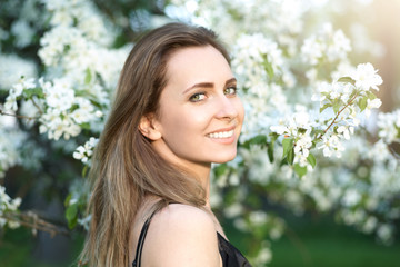 Fototapeta premium Pretty in establishment of branches of a blossoming apple. Portrait of face young beautiful woman holding apple on Spring blooming apple tree background summer nature. spring season