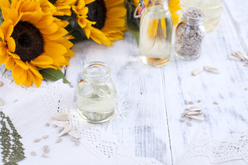 Sunflower oil and large yellow flowers. Oil in the bottle. Without peel of sunflower seeds and cookies. White wooden background. Vintage photo. Organic food. Copy space.