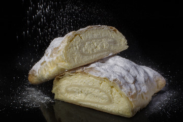 Strudel with cottage cheese sprinkled with powdered sugar cut close-up on a black background