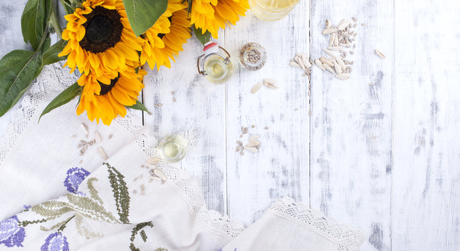 Sunflower oil and large yellow flowers. Oil in the bottle. Without husks of sunflower seeds. White wooden background. Vintage photo. Organic food.