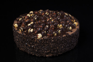 Chocolate cake with hazelnuts with white cream on a black background closeup