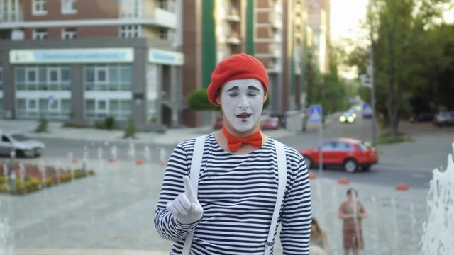 Funny mime in red beret show thumb up at fountain background